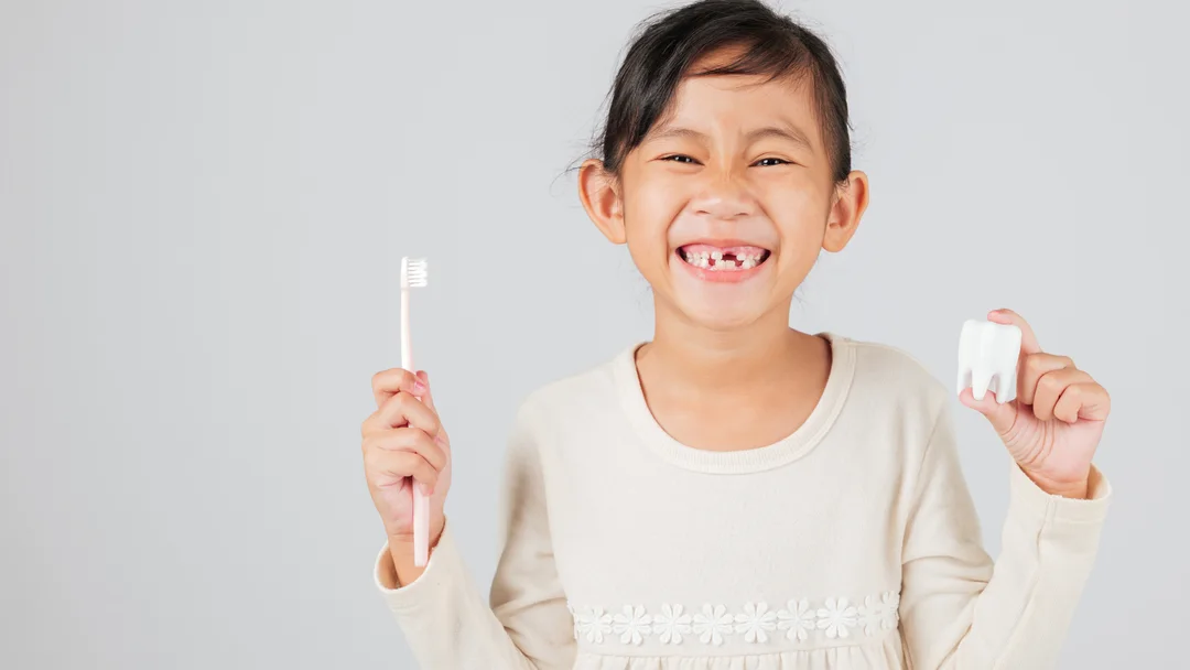 A young patient smiling at Portage Dental Group, holding a toothbrush and a model tooth